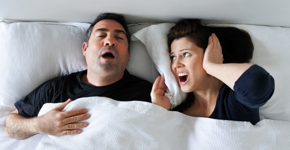 Woman frustrated in bed next to snoring man