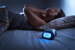 Woman laying in bed struggles to fall asleep as clock shows the time