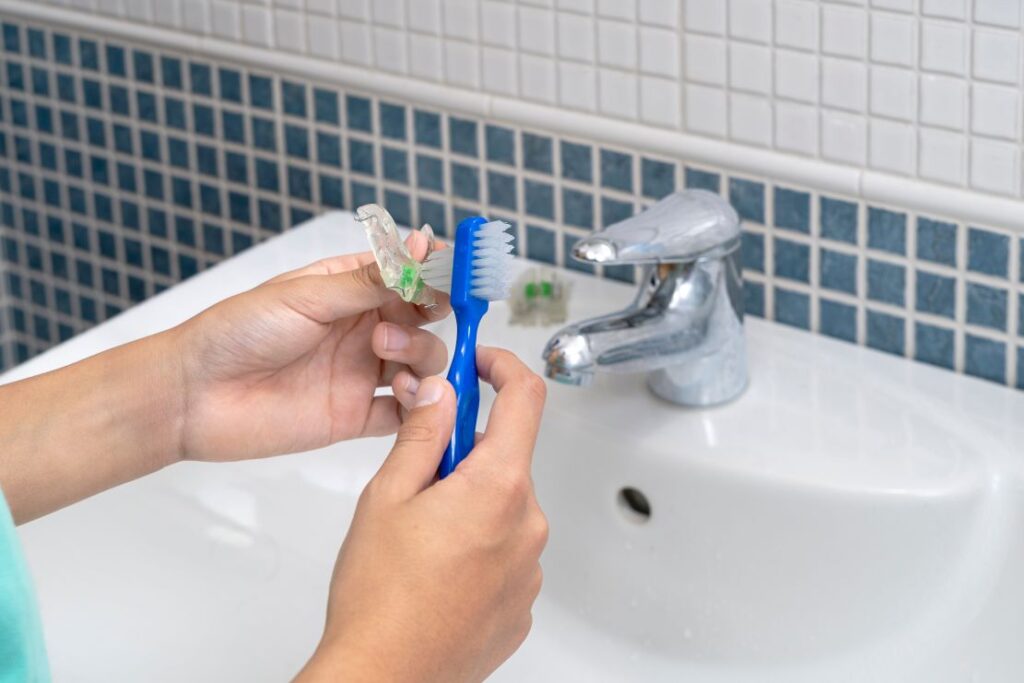 A person cleaning their oral sleep appliance with a toothbrush